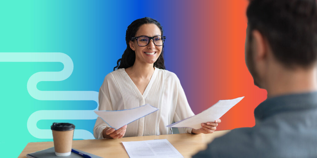 A smiling business woman holding papers and talking with a business man at a table, on top of a bright gradient background.