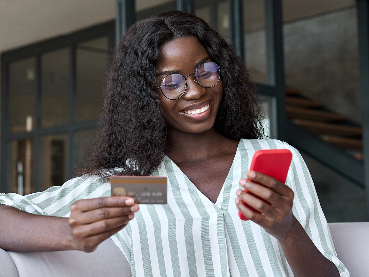 A woman smiling and using a credit card to buy something on her phone.