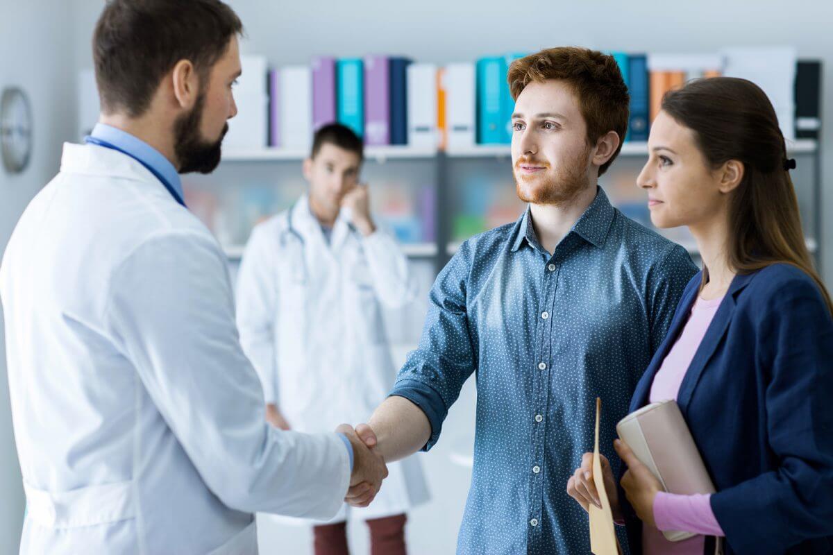 GroupHEALTH-CaseStudy-Header A doctor shaking a couple's hand and giving them a document.
