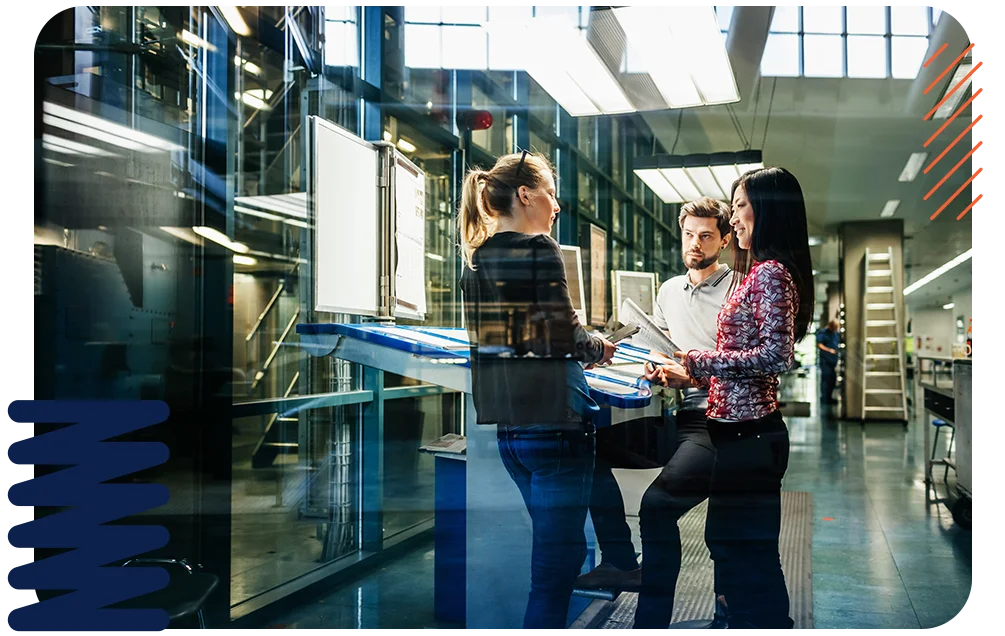 A group of colleagues discussing a project on a factory floor.