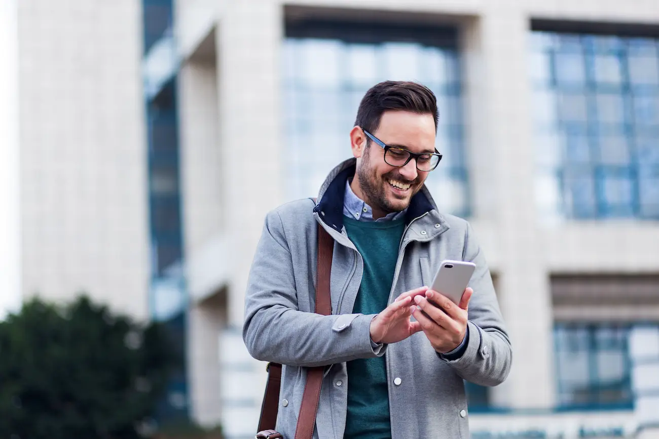 experlogix-mobile-sales-rep-app-for-intact-v3 A man smiling outside his office and looking at his phone.