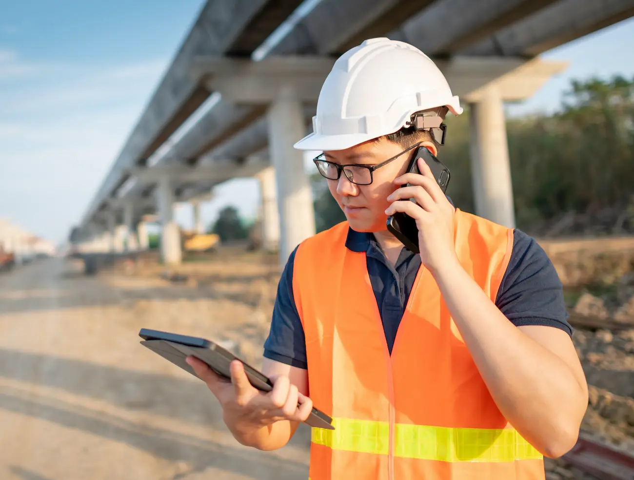 navigating-the-digital-shift-how-e-commerce-and-mobile-apps-transform-builders-merchants A man in a hard hat calling someone on his phone while looking at a tablet.
