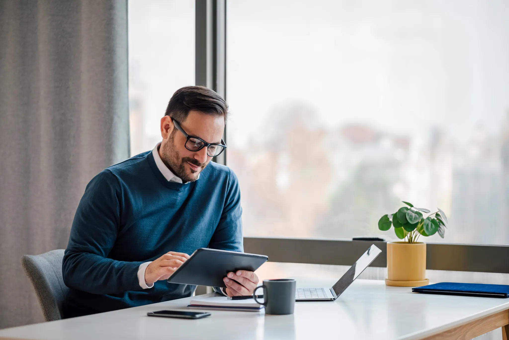 shutterstock_2180173613 A man sitting at his desk using some devices, working.